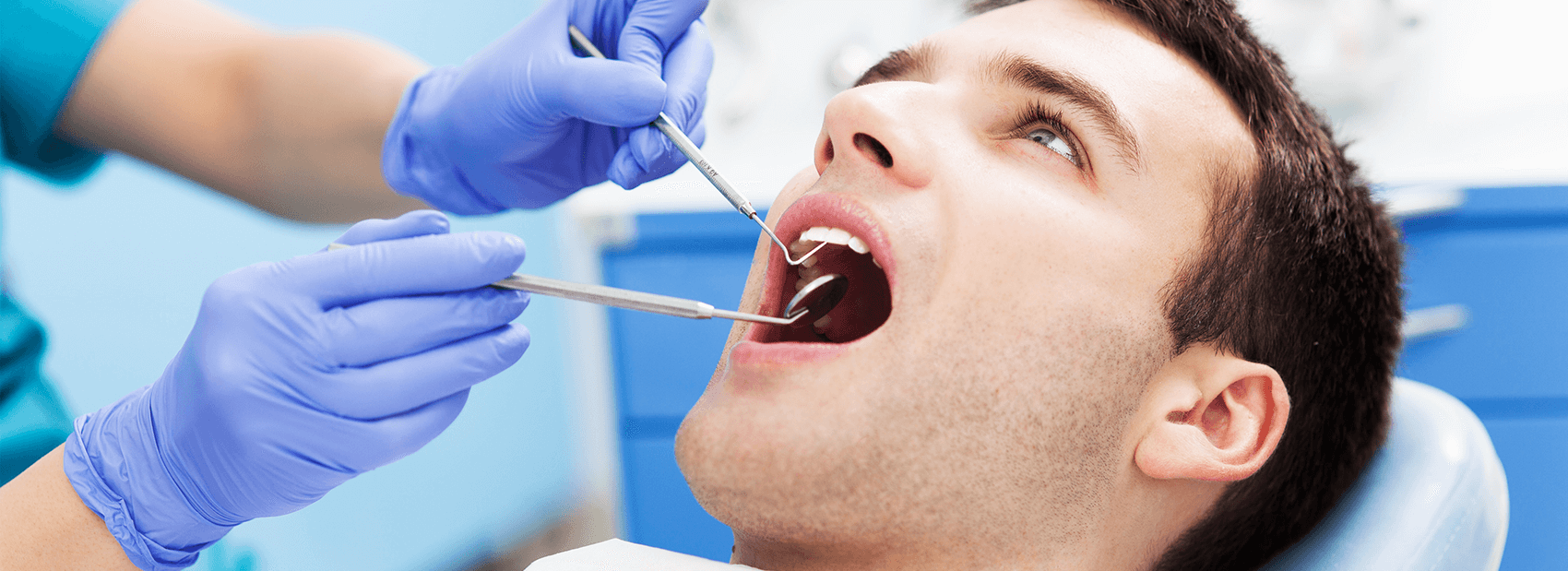 Man laying back and dental chair with his mouth open while the hygienist begins an exam