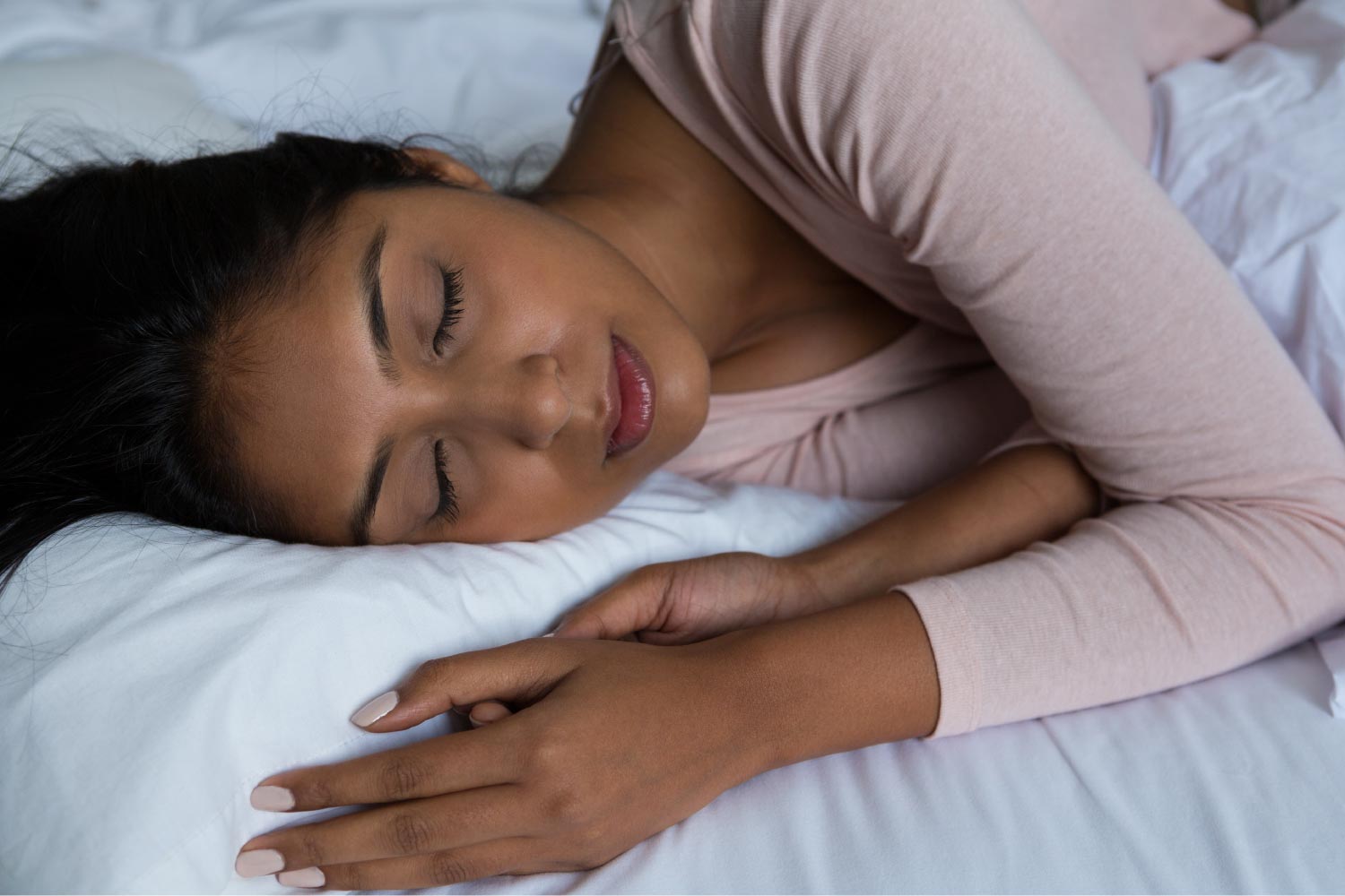 Woman in a pink shirt sleeps soundly while wearing a sleep apnea appliance from her Fort Smith dentist