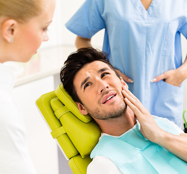 man holding his jaw in pain while talking to his dentist