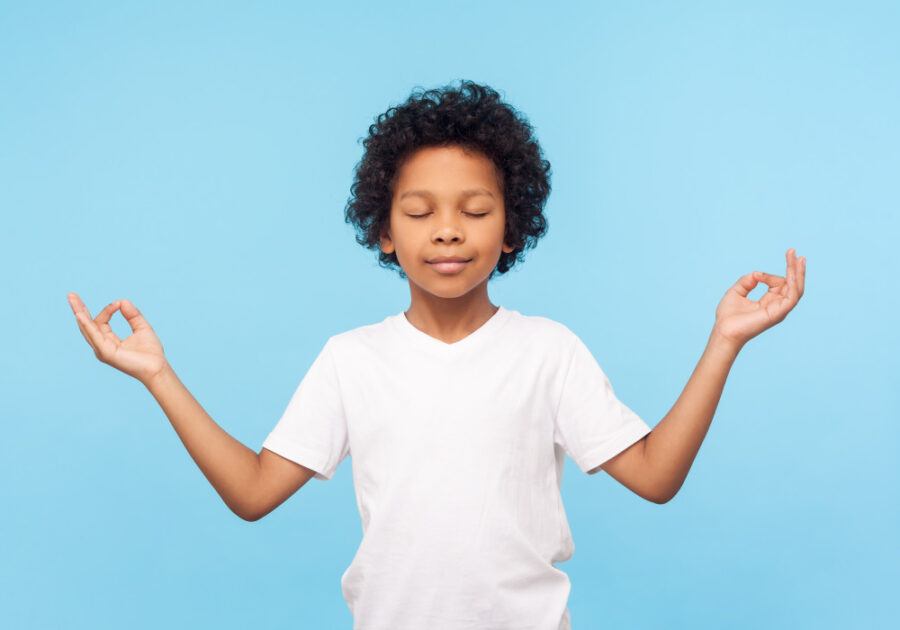 Black boy in a white t-shirt against a sky blue wall relaxes in an ohm zen pose thanks to dental sedation