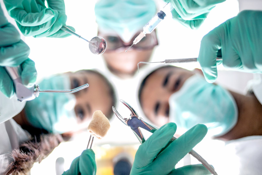 Looking up into masked dentists performing oral surgery with special tools in teal scrubs