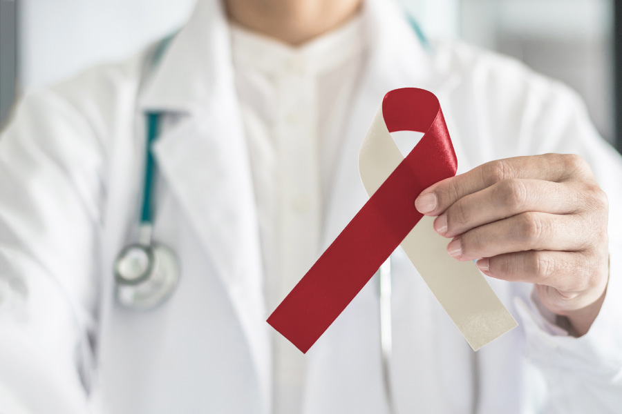 Closeup of a dentist in a white coat holding up a beige and red ribbon to indicate oral cancer awareness