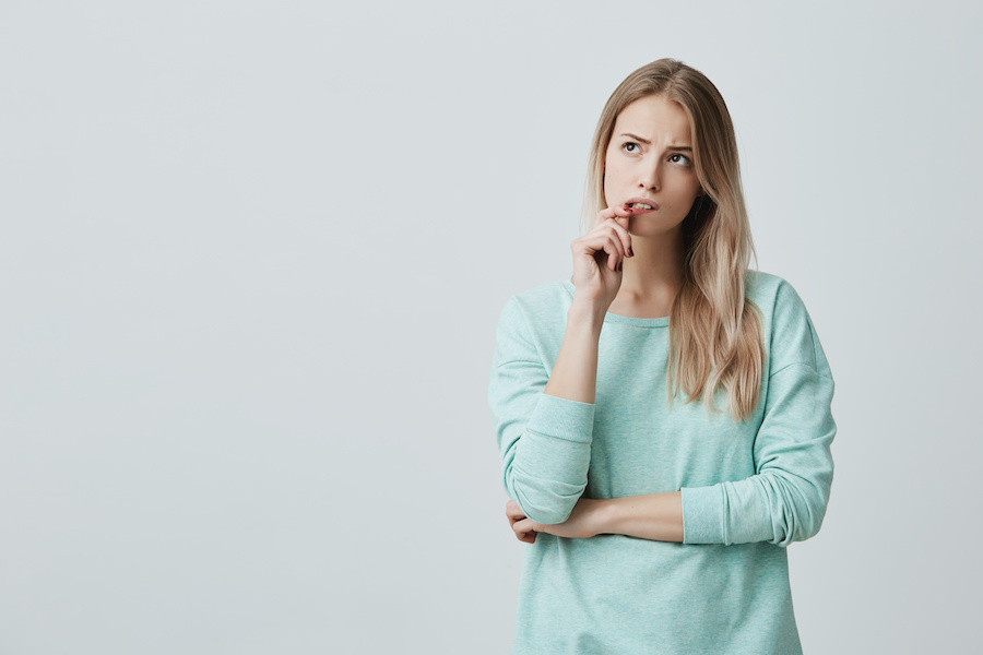 Blonde woman in a turquoise sweater pulls at her lip and looks wonderingly