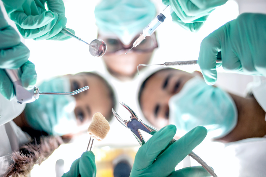 Looking up into the masked faces of 3 dental professionals holding oral surgery tools