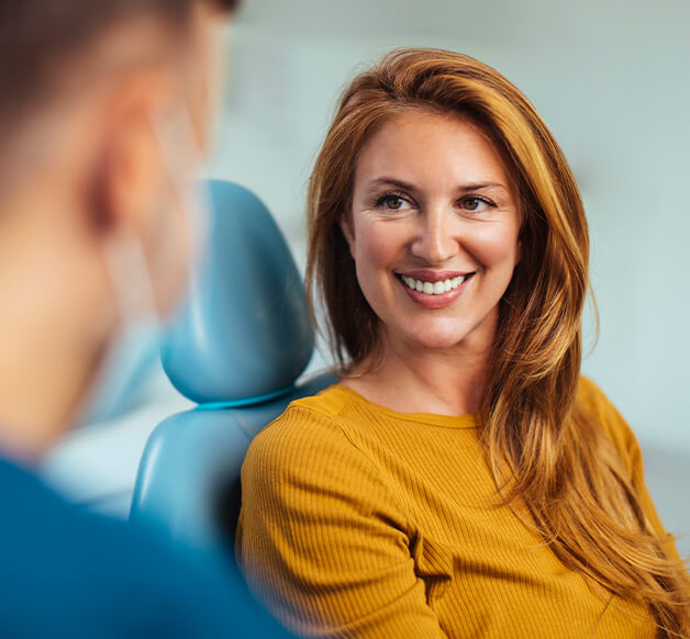 smiling woman sitting in a dental chair, talking with her dentist