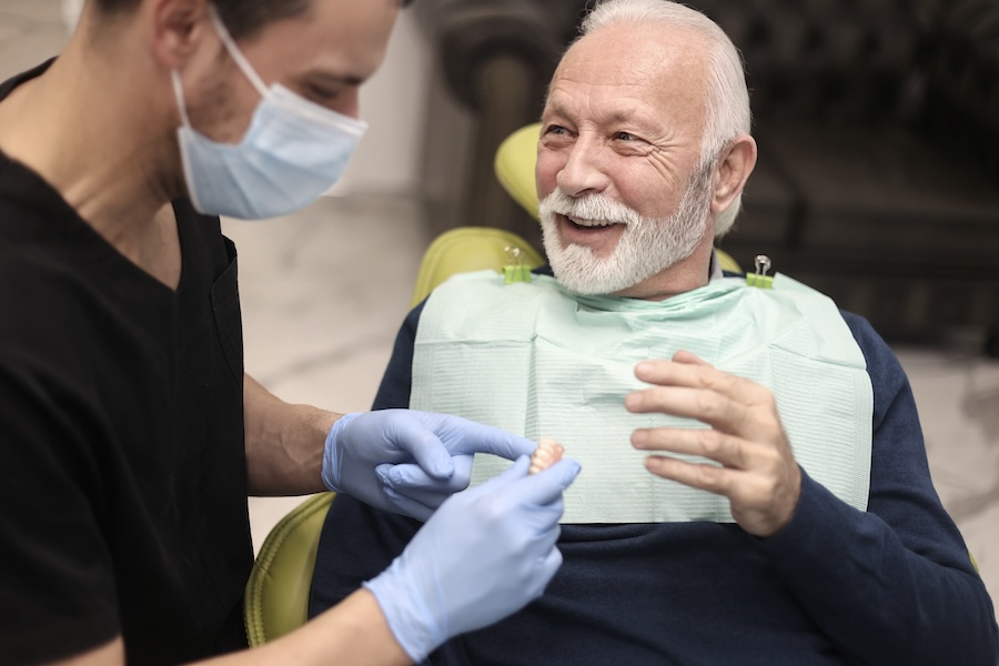 senior man in dental chair discussing dentures and dental implants for missing teeth